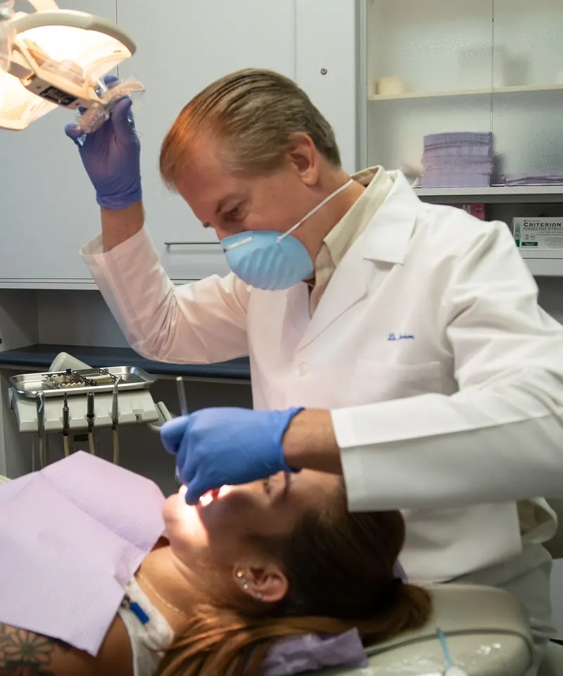 A Harrison Dental Group dentist in a mask and gloves treating a patient in the chair.