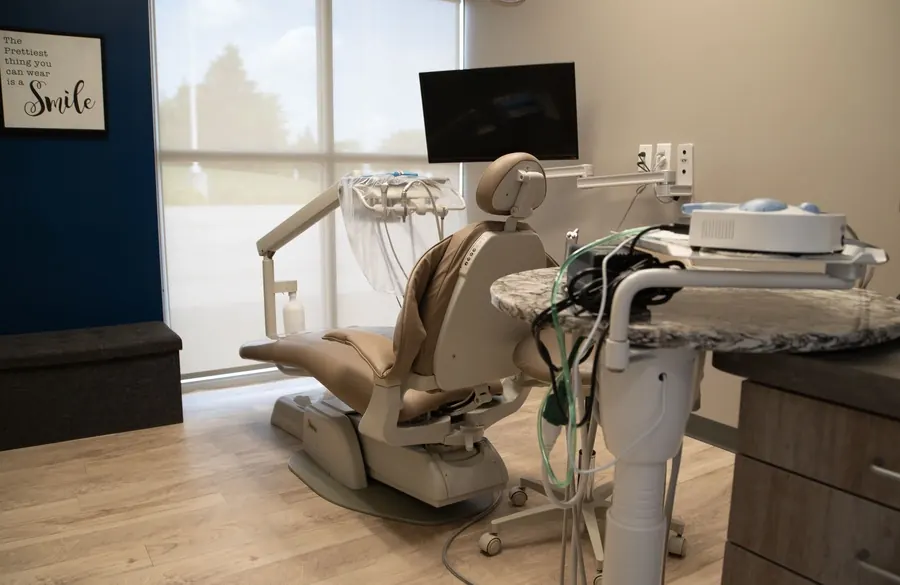 A bright treatment room with a dental chair and a wall-mounted screen.