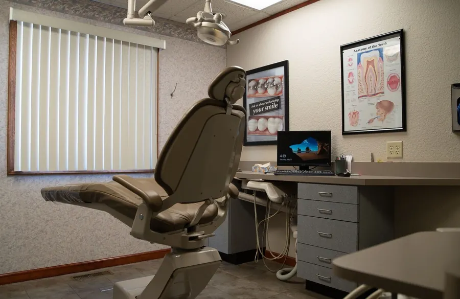 A treatment room with a reclining dental chair, a computer and educational posters.