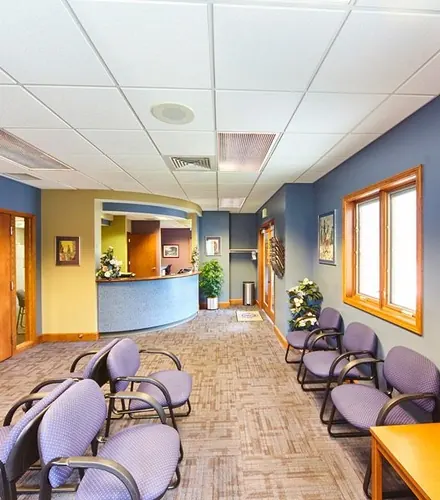 A long waiting room with a blue wall, rows of chairs and the front desk at the far end.