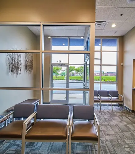 A waiting area with brown leather chairs beside a tall window and a glass entrance door.