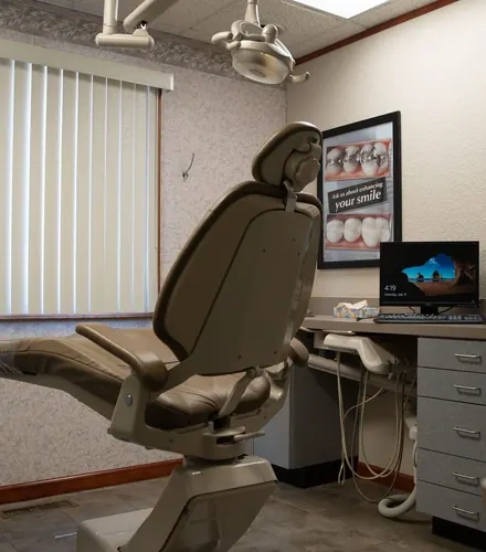 A treatment room with a dental chair, a computer and a smile poster on the wall.