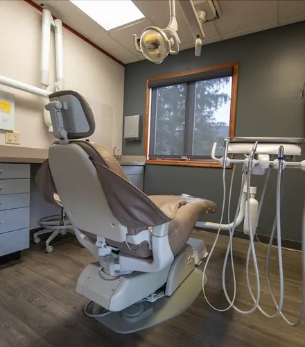 A treatment room with a dental chair, overhead light and a window.