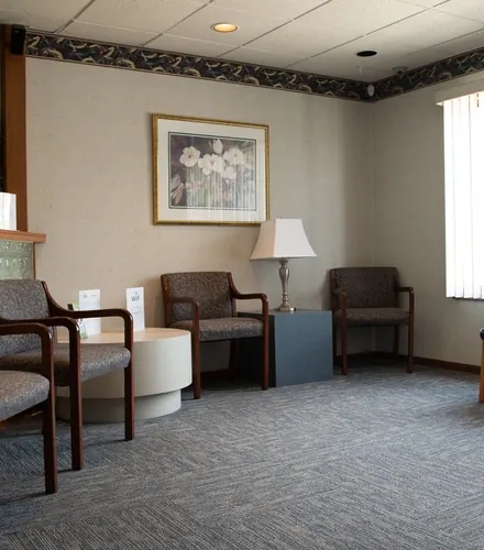 A waiting room with upholstered chairs, lamps and framed art.